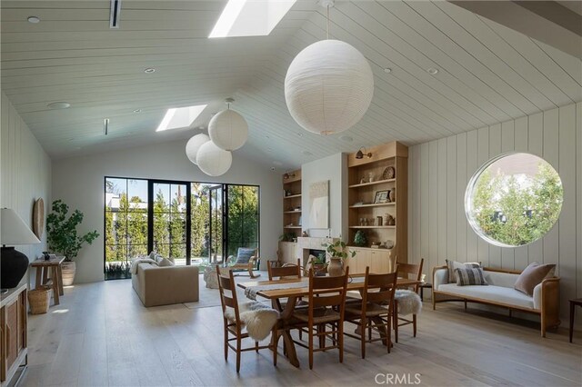 dining area with built in shelves, lofted ceiling with skylight, wood walls, and light hardwood / wood-style floors