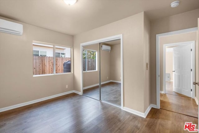 unfurnished bedroom featuring hardwood / wood-style floors, a closet, and a wall mounted air conditioner