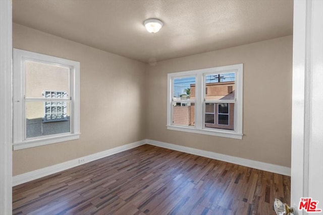 empty room featuring dark wood-type flooring and a healthy amount of sunlight