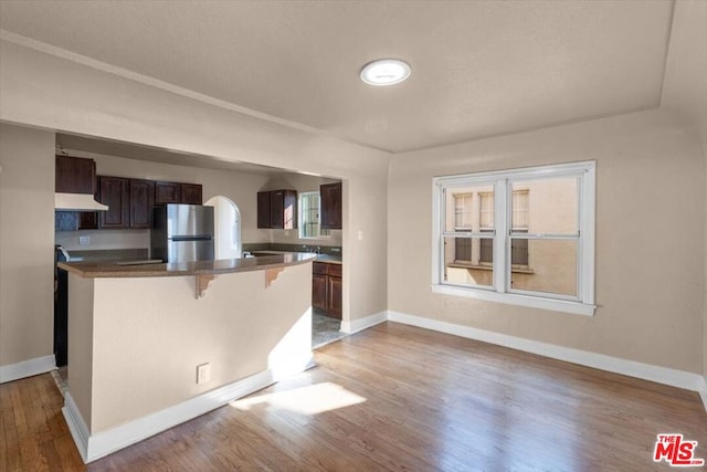 kitchen with a kitchen bar, hardwood / wood-style flooring, dark brown cabinets, and stainless steel refrigerator