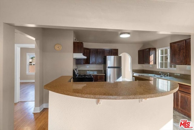 kitchen with sink, black gas stove, a kitchen breakfast bar, kitchen peninsula, and stainless steel refrigerator