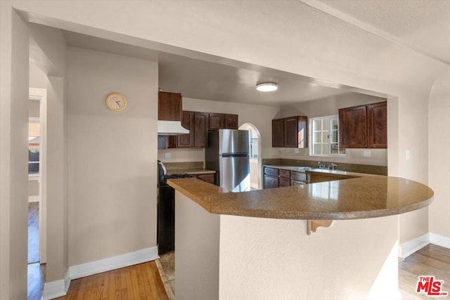 kitchen featuring stainless steel fridge, light hardwood / wood-style flooring, kitchen peninsula, and a breakfast bar area