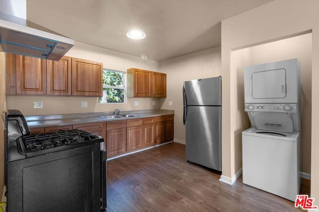 kitchen featuring stacked washer / drying machine, gas stove, sink, ventilation hood, and stainless steel fridge