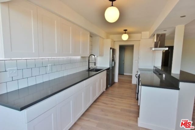 kitchen featuring white cabinetry, light hardwood / wood-style floors, decorative backsplash, wall chimney range hood, and sink