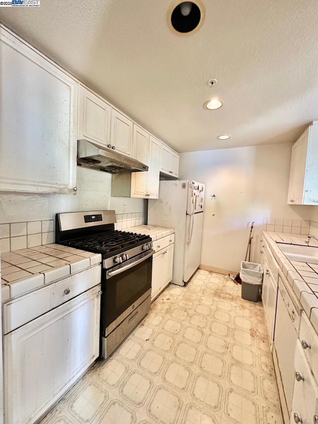 kitchen with white refrigerator, tile countertops, a textured ceiling, white cabinets, and stainless steel range with gas cooktop