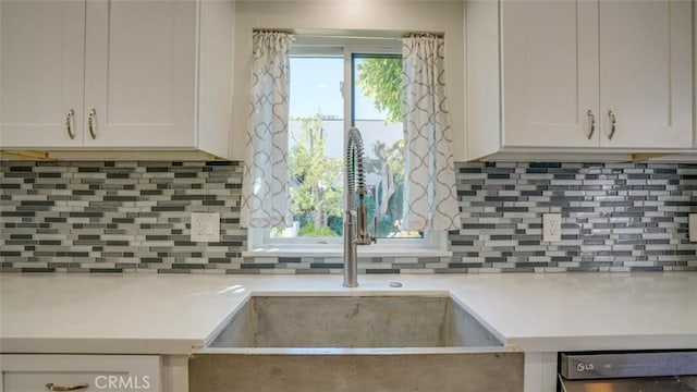 kitchen featuring dishwashing machine, sink, decorative backsplash, and white cabinets