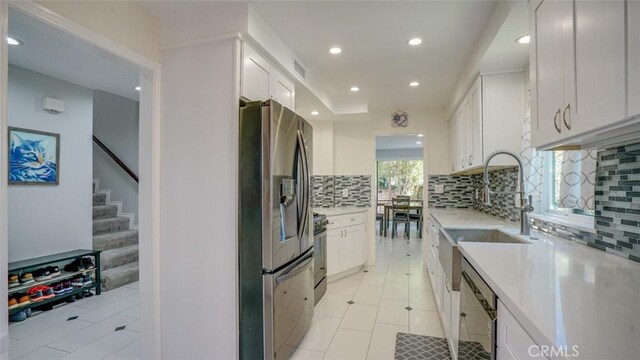 kitchen featuring dishwashing machine, light tile patterned floors, white cabinetry, stainless steel refrigerator with ice dispenser, and tasteful backsplash