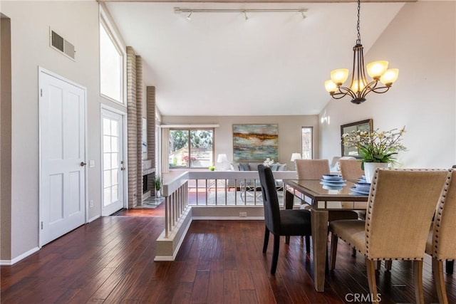 dining space featuring dark wood-type flooring, rail lighting, a chandelier, and high vaulted ceiling