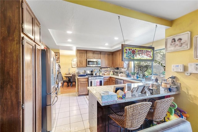 kitchen featuring a kitchen bar, kitchen peninsula, stainless steel appliances, light tile patterned flooring, and sink