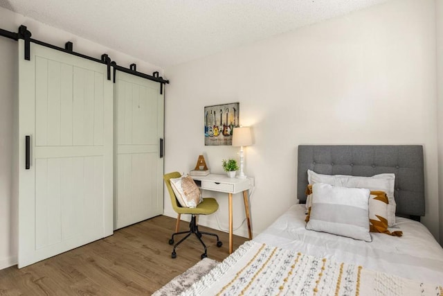 bedroom with a barn door, hardwood / wood-style floors, and a textured ceiling