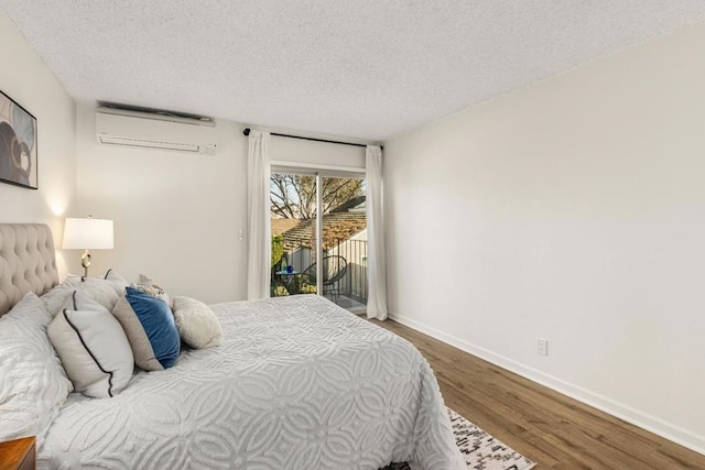 bedroom featuring access to exterior, hardwood / wood-style flooring, a wall unit AC, and a textured ceiling