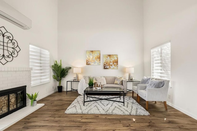 living room featuring a brick fireplace, dark wood-type flooring, a wealth of natural light, and a wall mounted AC