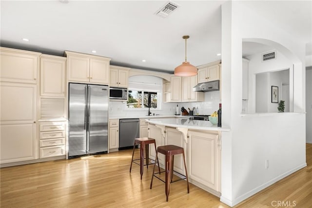 kitchen featuring cream cabinetry, tasteful backsplash, decorative light fixtures, light wood-type flooring, and built in appliances