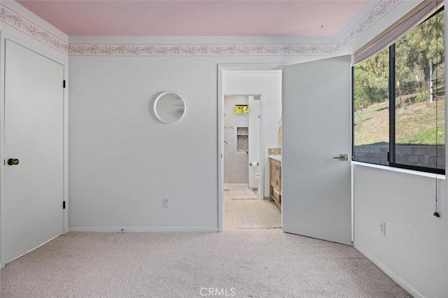 unfurnished bedroom with ensuite bathroom, light colored carpet, and multiple windows