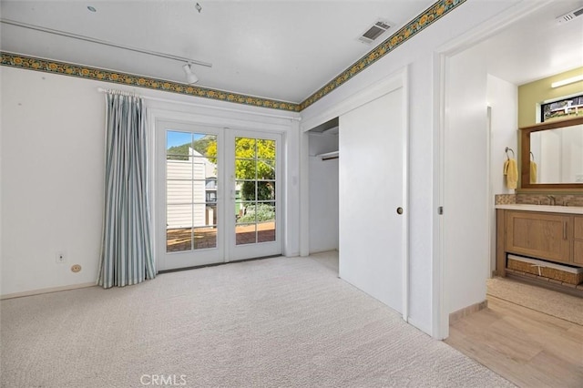 carpeted empty room with french doors, sink, and rail lighting