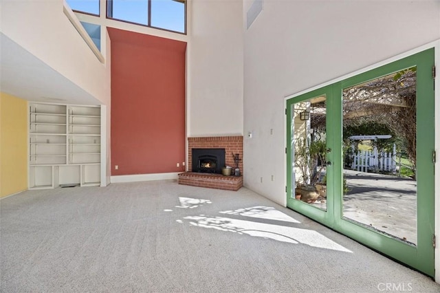 unfurnished living room with a brick fireplace, a towering ceiling, and carpet flooring