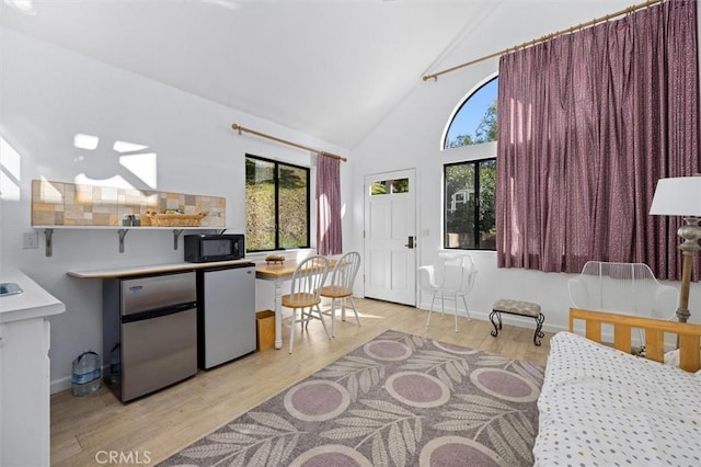 bedroom with light wood-type flooring, stainless steel refrigerator, and multiple windows