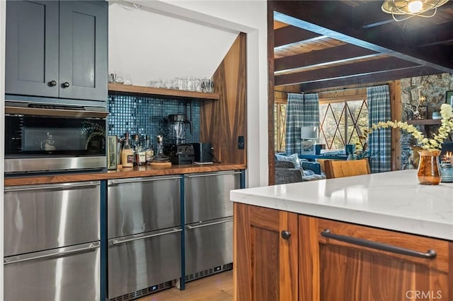 bar with light stone countertops, decorative backsplash, and stainless steel fridge