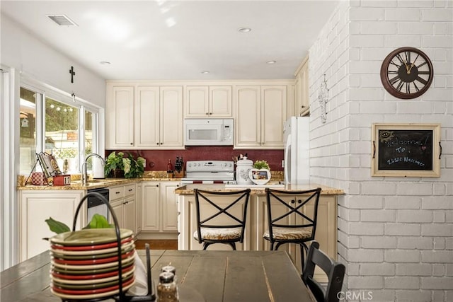 kitchen with light stone counters, white appliances, a kitchen breakfast bar, and cream cabinets