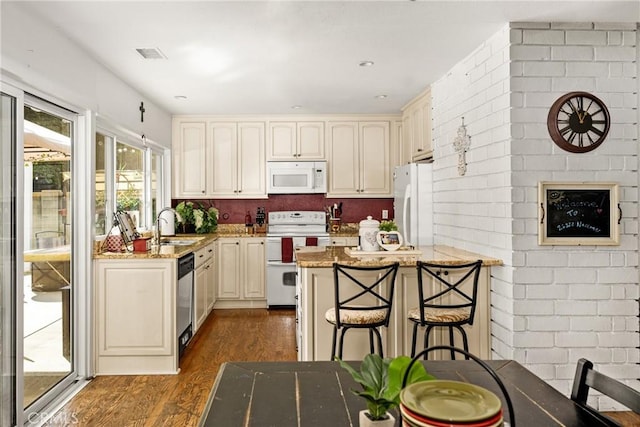 kitchen with dark hardwood / wood-style floors, sink, a kitchen breakfast bar, light stone counters, and white appliances