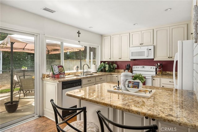 kitchen featuring sink, white appliances, a breakfast bar area, light stone counters, and light wood-type flooring