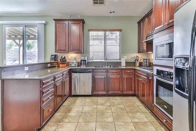 kitchen with stainless steel appliances, dark stone counters, sink, kitchen peninsula, and light tile patterned floors