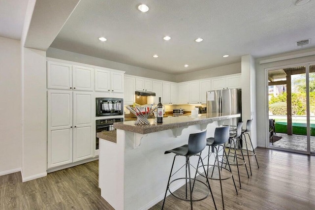 kitchen featuring dark hardwood / wood-style floors, black appliances, a kitchen bar, white cabinetry, and an island with sink