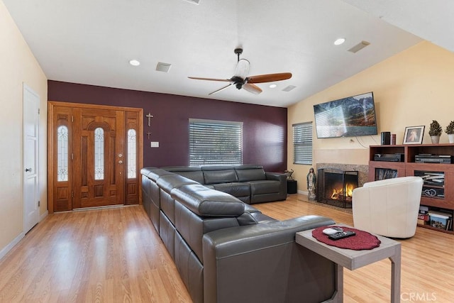 living room featuring a fireplace, lofted ceiling, ceiling fan, and light wood-type flooring