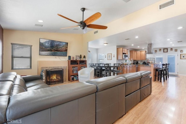 living room with a fireplace, lofted ceiling, ceiling fan, and light wood-type flooring