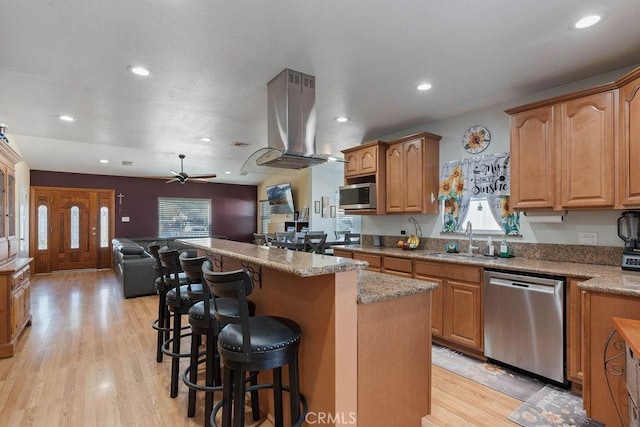 kitchen featuring a center island, sink, island exhaust hood, appliances with stainless steel finishes, and a breakfast bar area