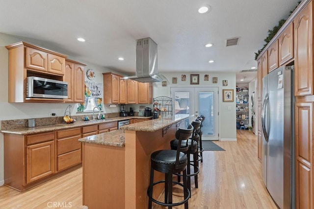 kitchen featuring island range hood, stainless steel appliances, a kitchen breakfast bar, light wood-type flooring, and a kitchen island