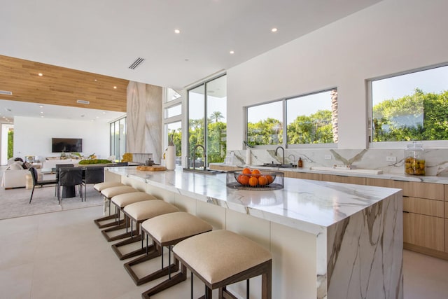 kitchen with tasteful backsplash, a spacious island, a breakfast bar, sink, and light stone countertops