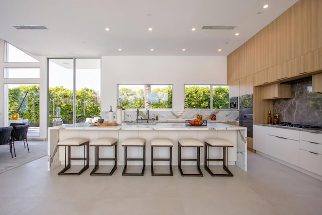 kitchen with a breakfast bar, decorative backsplash, a large island, white cabinets, and light stone counters