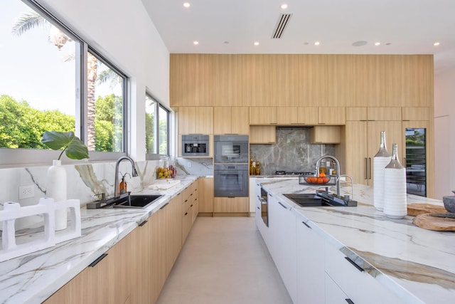 kitchen featuring double oven, decorative backsplash, sink, and light stone counters