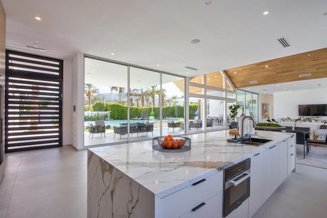 kitchen featuring light stone countertops, sink, a large island with sink, and white cabinets