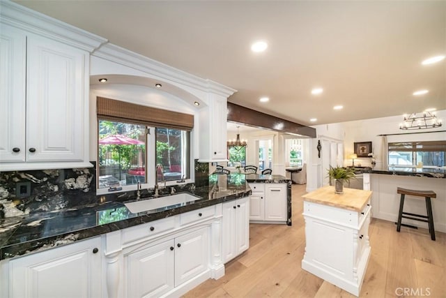 kitchen featuring decorative backsplash, white cabinets, a kitchen island, dark stone countertops, and sink