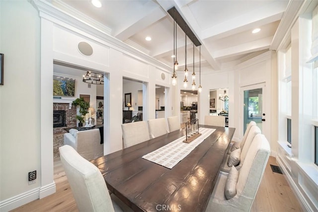 dining space featuring a brick fireplace, light hardwood / wood-style floors, beamed ceiling, and coffered ceiling