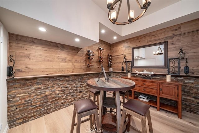 dining area with light hardwood / wood-style floors, a chandelier, and wooden walls