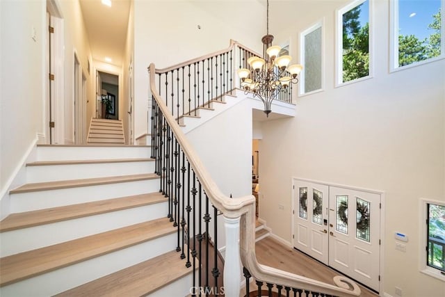 staircase with a notable chandelier, hardwood / wood-style flooring, and a towering ceiling