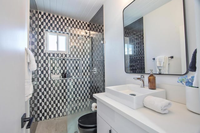 bathroom with toilet, tiled shower, and vanity