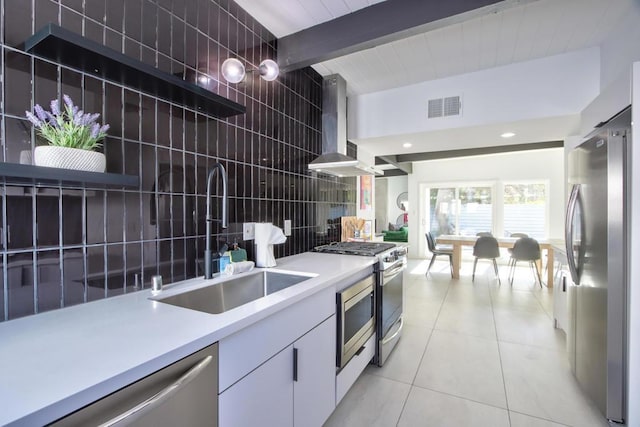 kitchen with wall chimney range hood, beam ceiling, sink, appliances with stainless steel finishes, and white cabinets