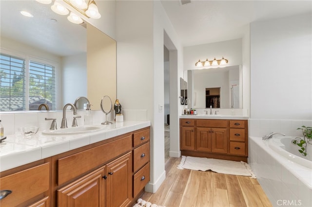 bathroom with hardwood / wood-style flooring, a relaxing tiled tub, and vanity