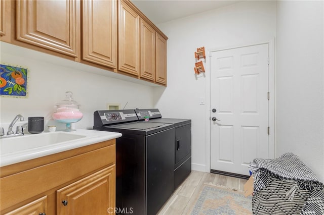 clothes washing area with washer and dryer, light hardwood / wood-style floors, sink, and cabinets