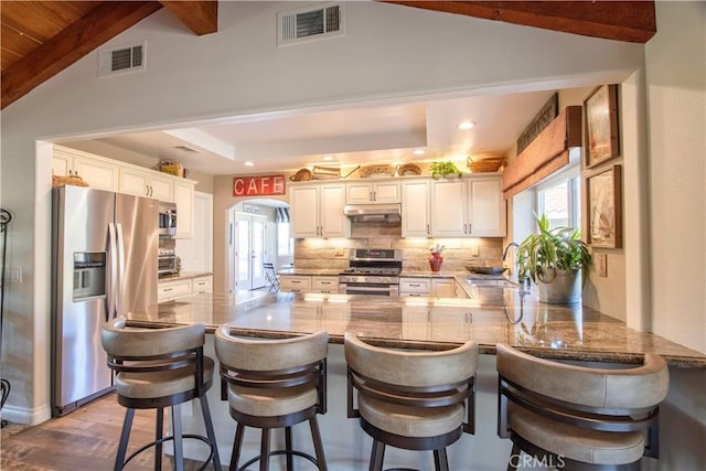 kitchen featuring a kitchen bar, kitchen peninsula, stainless steel appliances, backsplash, and sink