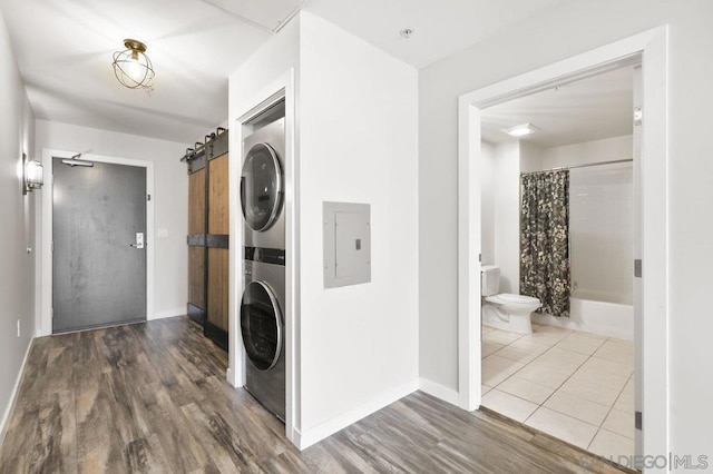 washroom with a barn door, stacked washer and dryer, hardwood / wood-style flooring, and electric panel