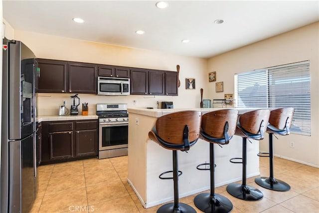 kitchen with dark brown cabinetry, light tile patterned floors, stainless steel appliances, and a kitchen breakfast bar