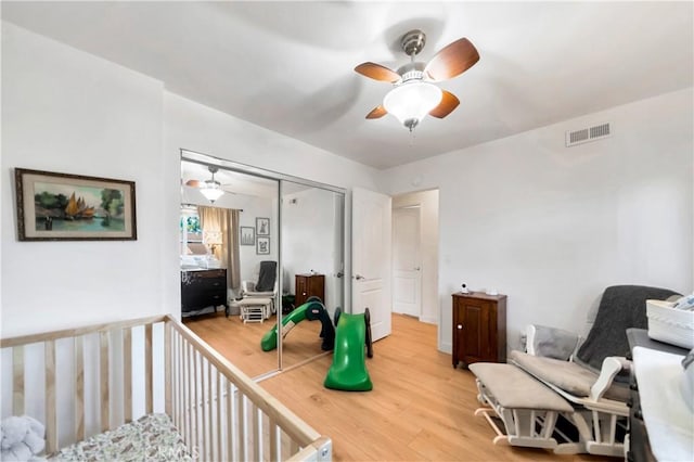 bedroom featuring ceiling fan, a nursery area, hardwood / wood-style flooring, and a closet