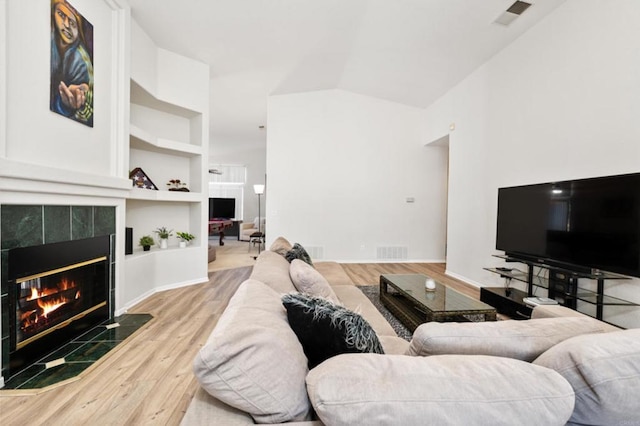 living room with lofted ceiling, a tiled fireplace, light hardwood / wood-style floors, and built in features