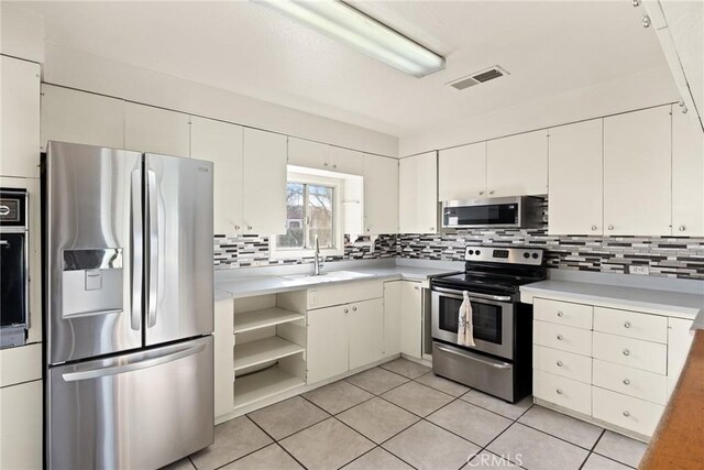 kitchen with backsplash, sink, light tile patterned flooring, stainless steel appliances, and white cabinets