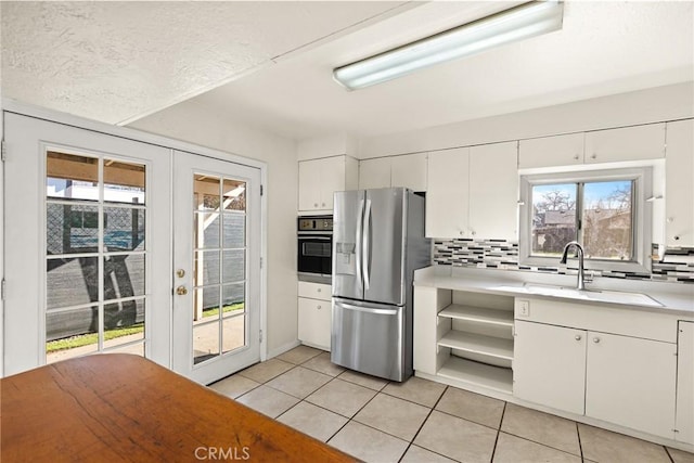 kitchen featuring stainless steel refrigerator with ice dispenser, white cabinetry, sink, oven, and light tile patterned floors